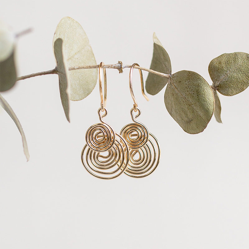 aretes espiral dorados sobre rama de eucalipto verde y sobre fondo blanco