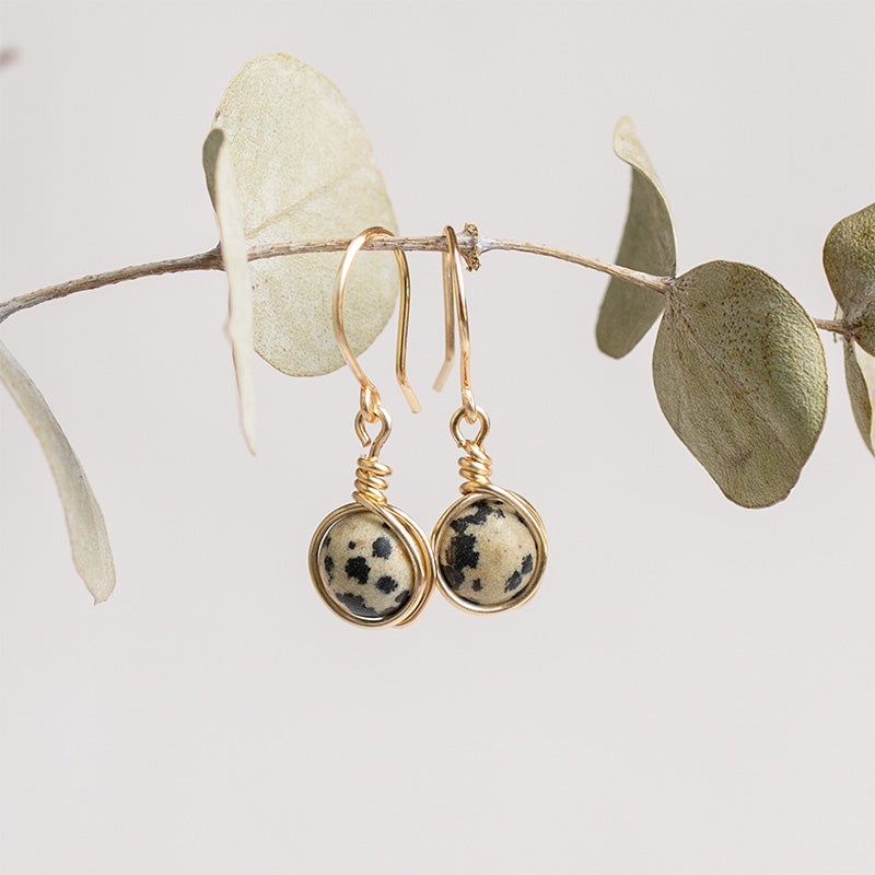 Aretes dorados con jaspe dálmata sobre rama con hojas.