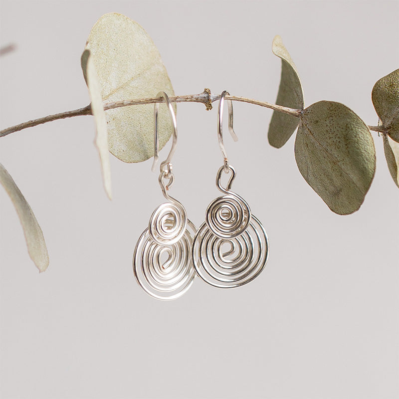 aretes espiral plateados sobre rama de eucalipto verde y sobre fondo blanco