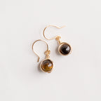 Aretes dorados con piedras marrones sobre fondo blanco