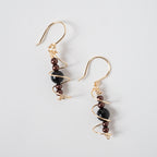 Par de aretes dorados en espiral con cuentas negras y marrones sobre un fondo claro.