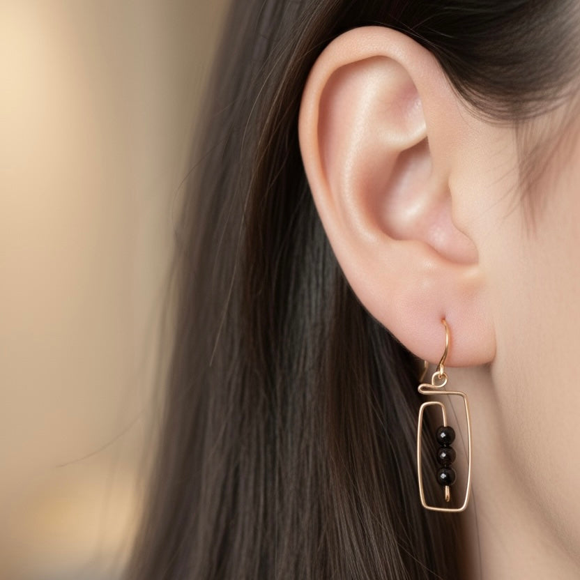 Oreja con arete dorado y cuentas negras, fondo desenfocado.